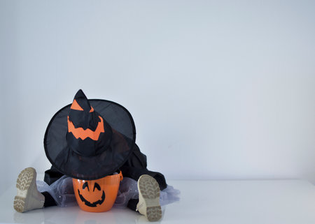 little girl dressed as a witch sticking her head in her halloween basket, white backgroundの写真素材