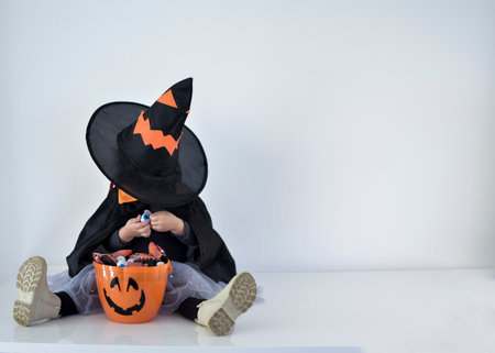 Little girl dressed as a witch looking for candy in her halloween basket, white backgroundの写真素材