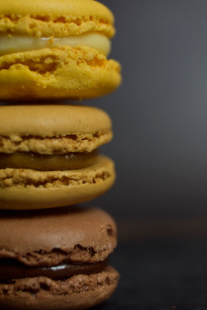 Brown and yellow toned macarons stacked on black background, close upの写真素材