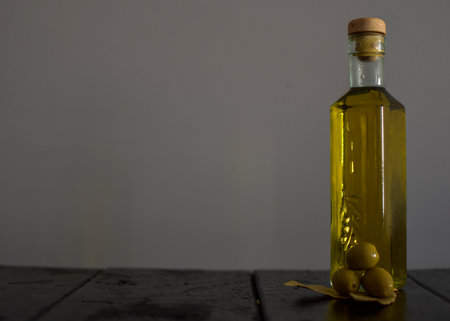 Glass bottle with olive oil, olives and olive leaves on black wooden table.の写真素材