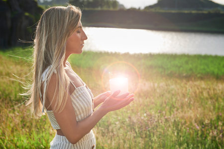 Blonde girl practicing meditation with a candle at dawnの写真素材