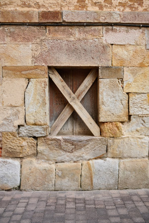 Close up view of stone facade with wooden window blocked with two x-shaped wooden slatsの写真素材