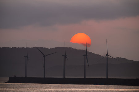 Wind turbines are generating clean energy against the backdrop of a dawn in the Bilbao port, Biscay,...