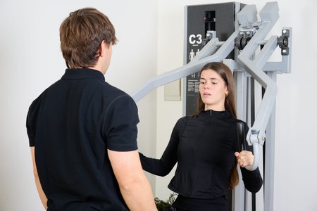 Young woman working out on a chest press machine, focused on building strength under the guidance of...