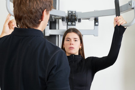 Personal trainer supervising a young woman performing an exercise on a chest press machine at the...