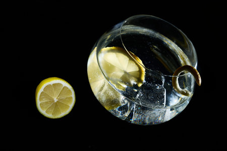 Clear cocktail with lemon slice, ice cubes, and a peel garnish against a dark background, ready for...