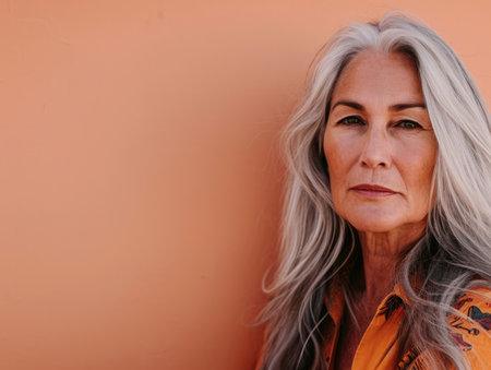 Close up of a confident middle aged woman with a peach copyspace backgroundの素材