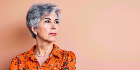 Close up of a confident middle aged woman with a peach copyspace backgroundの素材
