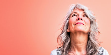Close up of a confident middle aged woman with a peach copyspace backgroundの素材