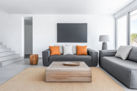 A contemporary living area showcases gray couches adorned with orange cushions, a wooden coffee table, and abundant natural light streaming through large windows.の素材