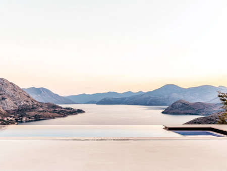 A stunning view at sunset showcases a serene bay bordered by mountains, with a sleek infinity pool merging with the horizon, creating a relaxing atmosphere.の素材