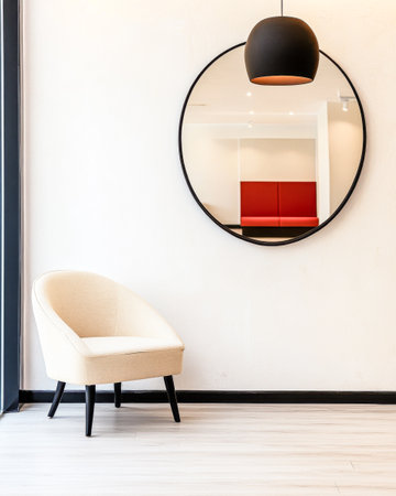 A cozy cream armchair sits beside a large round mirror on a light-colored wall, complemented by warm lighting and sleek wooden flooring in a contemporary setting.の素材