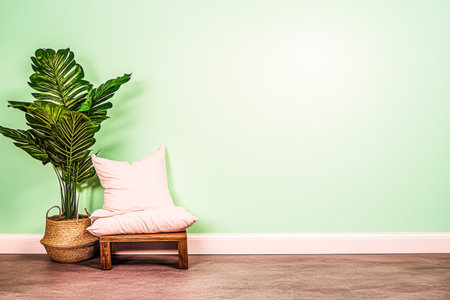 A serene corner features a vibrant green wall and a potted plant beside a wooden stool, adorned with a soft pillow, creating a relaxing ambiance.の素材