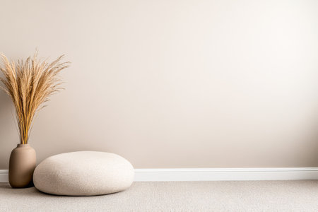 This tranquil space showcases a minimalist design with a beige wall, a unique vase holding dried grass, and a plush round pouf on a carpeted floor.の素材