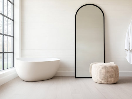 A sleek freestanding bathtub sits next to a large mirror in a minimalist bathroom. Soft natural light filters through a window, enhancing the serene atmosphere.の素材