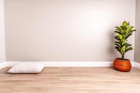 A soft pillow rests on a light wood floor beside a stylish potted plant, enhancing the serene ambiance of a minimalist living area with neutral tones.の素材