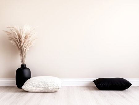 A stylish minimalist corner showcases a large cream pillow and a sleek black pillow on the floor, complemented by a modern vase filled with dried plants against a light-colored wall.の素材