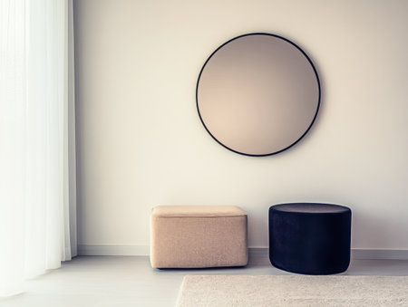 A minimalist living area showcases a large round mirror on the wall, paired with a beige and black pouf, highlighting sleek and modern decor.の素材