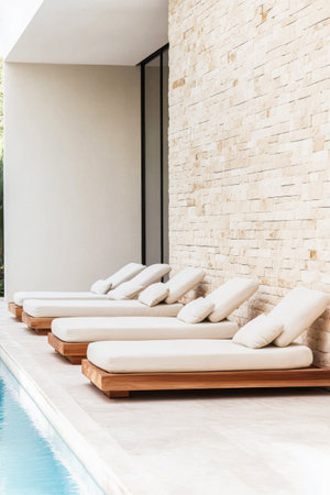 Four elegant loungers are arranged neatly beside a tranquil pool, featuring soft cushions that invite relaxation during sunny days in a sophisticated atmosphere.の素材