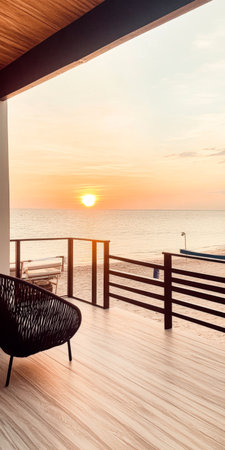 A tranquil sunset casts warm colors across the ocean from a beachfront balcony. The scene invites relaxation with its peaceful setting and soft waves.の素材