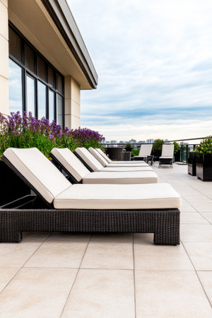 Comfortable lounge chairs line a modern rooftop terrace, surrounded by flowering plants, offering a serene spot to unwind while enjoying views of the city skyline.の素材