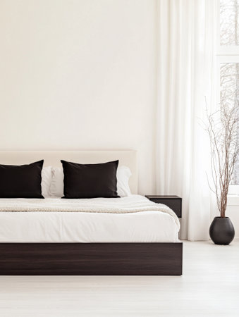 A spacious, modern bedroom features a large bed decorated with black pillows, a minimalist nightstand, and elegant plants adding a touch of nature to the bright room.の素材