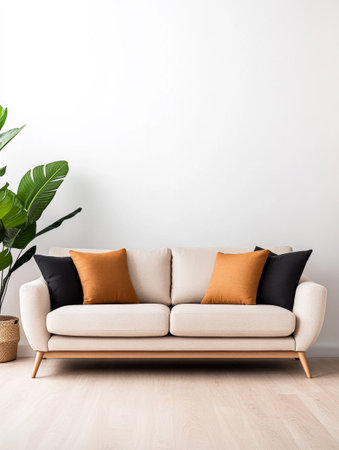A modern beige sofa is adorned with orange and black cushions, positioned against a simple white wall. A lush potted plant adds a touch of greenery to the minimalist decor.の素材
