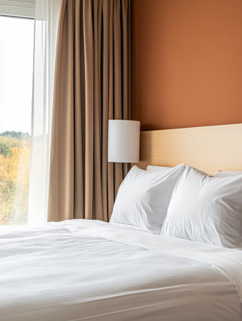 A well-appointed hotel room features a neatly made bed with white linens and soft pillows. Natural light streams in through a large window, illuminating warm wall colors and curtains.の素材