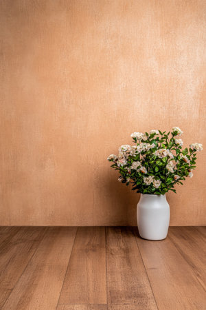 A white vase filled with fresh, blooming flowers stands elegantly on a wooden floor, complemented by a warm beige wall in the background, creating a cozy atmosphere.の素材