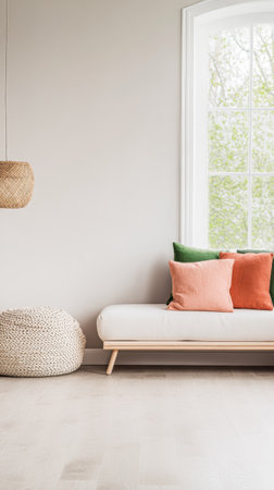 A bright living room features a minimalist white couch adorned with green and orange pillows. Natural light pours in through large windows, enhancing the tranquil atmosphere.の素材