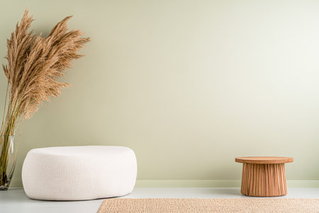 A contemporary living area showcases a cozy white pouf and a round wooden side table, complemented by dried pampas grass in a vase against a soft green wall.の素材