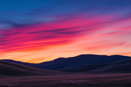 The sky is ablaze with hues of pink, purple, and orange as the sun sets behind gently rolling hills. The tranquil rural landscape creates a stunning backdrop for this beautiful evening display.の素材