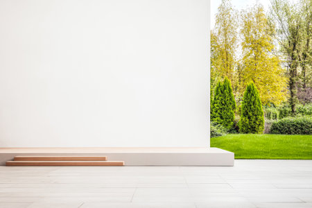 A bright interior showcases a clean white wall and wooden steps, seamlessly connecting to a lush green garden filled with trees under the clear blue sky.の素材