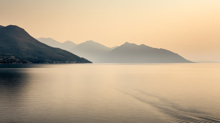 A serene landscape featuring calm waters reflecting a stunning sunset, with hazy mountains creating a tranquil atmosphere. This scene captures the essence of natural beauty.の素材
