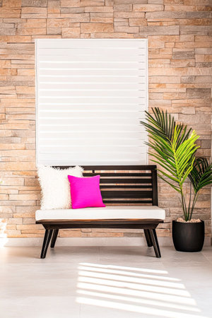 A cozy seating area features a sleek black bench adorned with a bright pink cushion, set against a textured stone wall. A green plant adds a refreshing touch to the decor.の素材