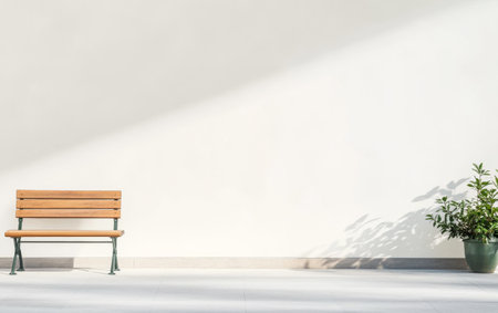 A wooden bench sits quietly next to a potted plant, casting soft shadows on a minimalist wall in a calm indoor area, creating a peaceful and inviting atmosphere.の素材