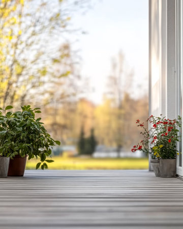 A wooden deck is adorned with potted green shrubs and blooming flowers, offering a peaceful view of an autumn landscape with colorful trees in the distance and soft golden light.の素材