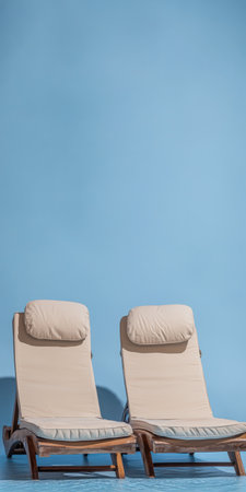 Two comfortable sun loungers are positioned side by side on a wooden deck, featuring plush headrests and set against a bright blue background, creating a peaceful retreat.の素材