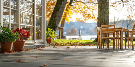 A charming outdoor dining space features wooden chairs and potted plants, set against a backdrop of autumn leaves by a tranquil lake in the late afternoon sun.の素材