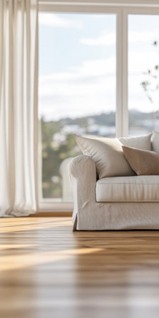 A bright and inviting living room features a comfortable light-colored sofa and decorative pillows. Large windows let in natural light and offer a beautiful outdoor view.の素材