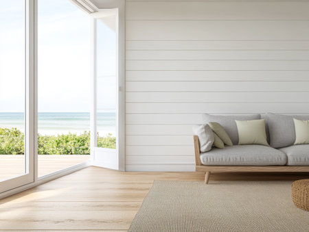 A bright living room features a comfortable sofa with cushions, an open door leading to a stunning ocean view, and soft wooden flooring, inviting fresh air and sunlight inside.の素材