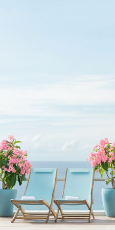 Two light blue lounge chairs are placed on a balcony overlooking the ocean, surrounded by vibrant pink flowers in pots under a clear sky.の素材