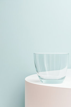 A clear glass bowl is placed on a simple white table, creating a serene ambiance with a soft blue wall in the background. The arrangement emphasizes minimalist design and elegance.の素材