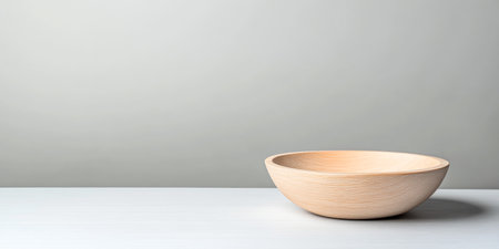 A wooden bowl sits on a clean white surface, illuminated by soft, diffused light, creating a serene and minimalistic atmosphere in the setting.の素材