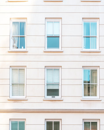 The exterior of a contemporary building features several windows, allowing sunlight to illuminate the interior. This urban landscape showcases a clean and minimalist design.の素材