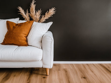 A cozy living room corner showcases a white sofa adorned with a brown accent pillow. Dried plants add a touch of nature against the dark wall, creating a warm, inviting atmosphere.の素材