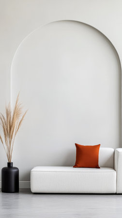 A sleek white sofa is positioned against a pale wall featuring an elegant arch. A dark vase holds tall decorative grasses, while a vibrant orange cushion adds a touch of color.の素材