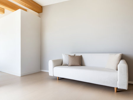 A contemporary living room features a stylish light-colored sofa with a decorative pillow. The space is bright and inviting showcasing neutral walls and wooden beams enhancing the modern atmosphere.の素材