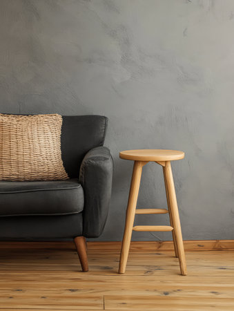 The living room features a stylish gray couch adorned with a woven pillow beside a simple wooden stool creating a warm and inviting atmosphere with textured wall and wooden floor.の素材