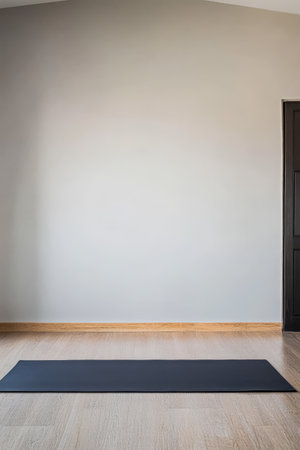 A spacious room features a black yoga mat on the wooden floor. The light-colored walls and simple decor reflect a calm atmosphere ideal for yoga or meditation sessions.の素材